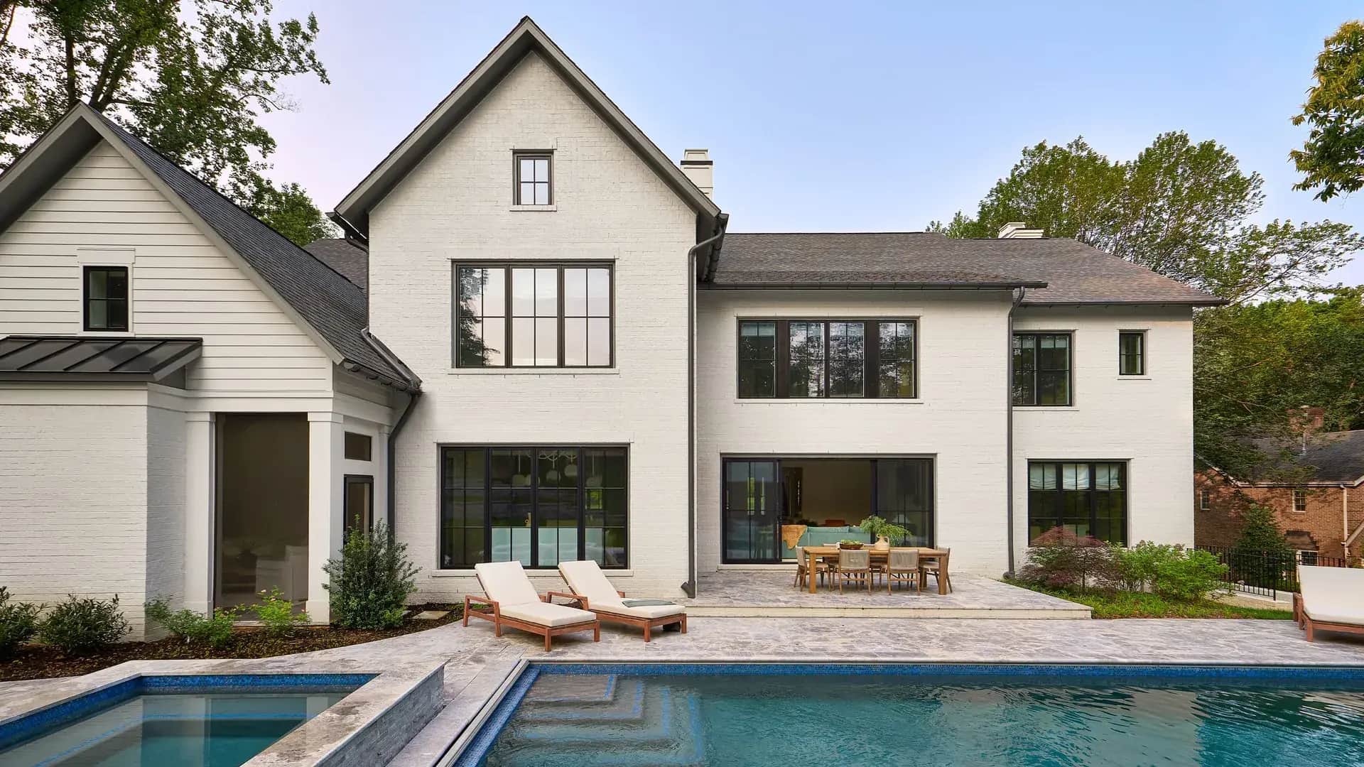 White-painted brick residence with dark window frames and pool terrace.