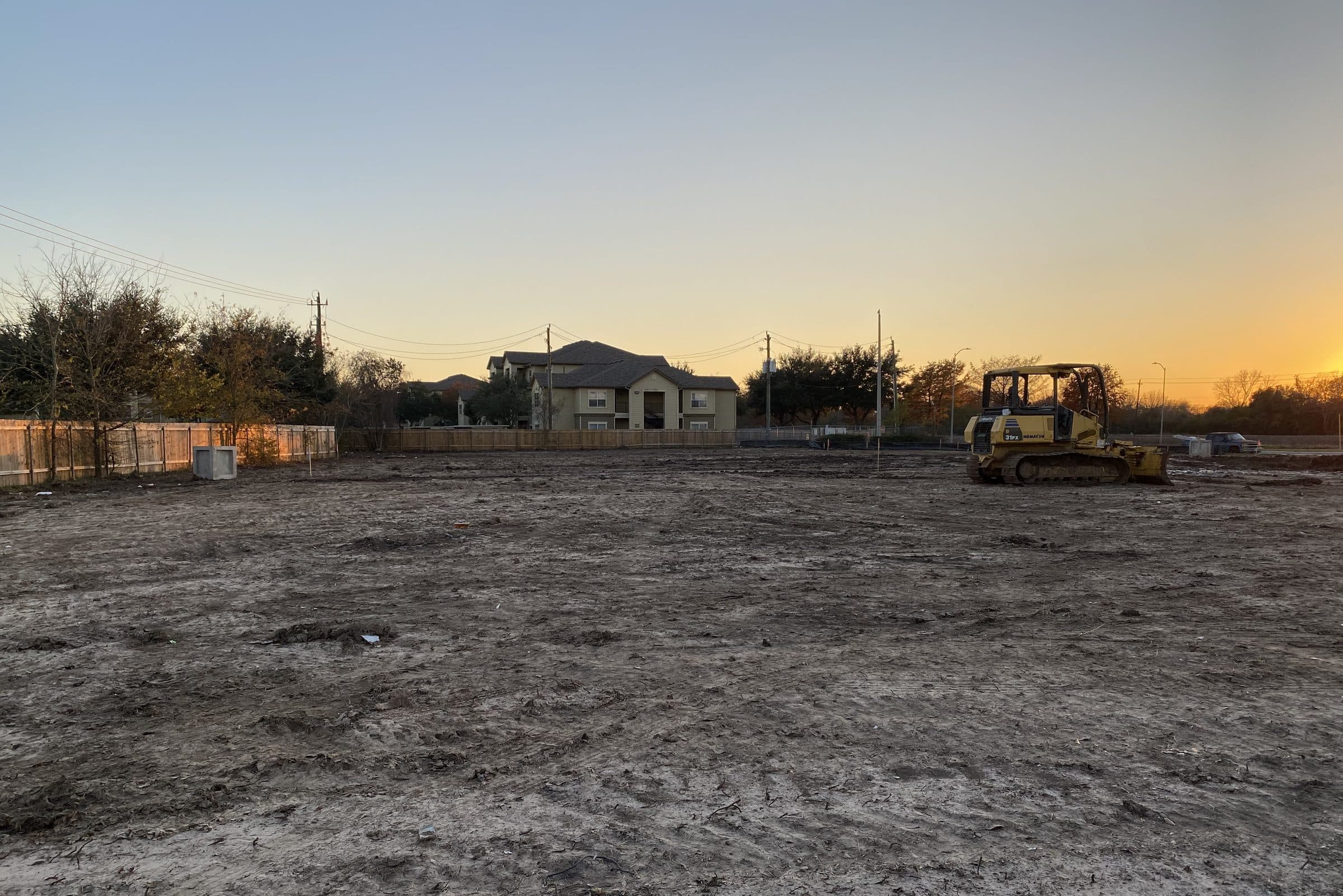 Cleared, graded lot at dusk with a dozer on site