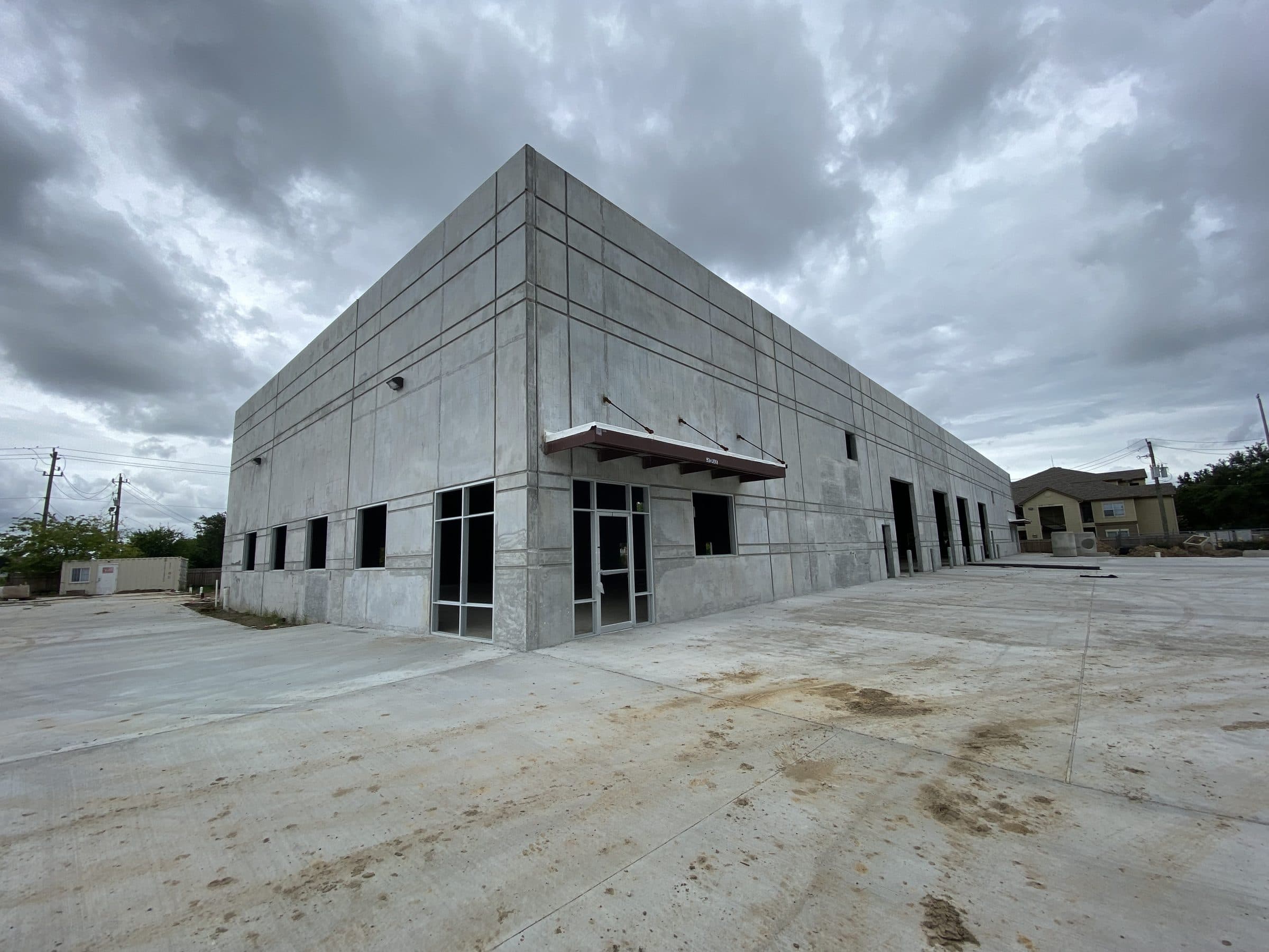 Completed tilt-wall shell with storefront glazing and paved approach